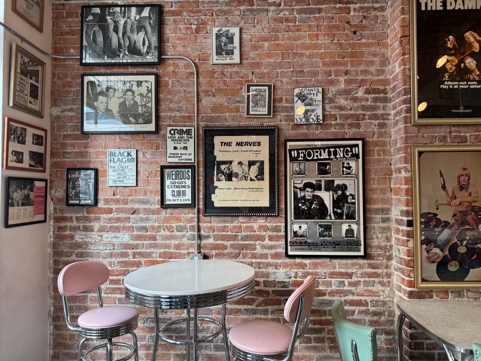 Vintage punk flyers and framed memorabilia on Funhouse’s brick wall, above tables and pink chairs